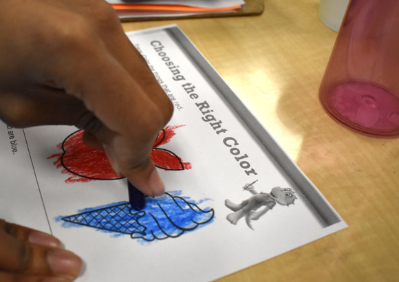 A child's hand hovers over a worksheet at his school