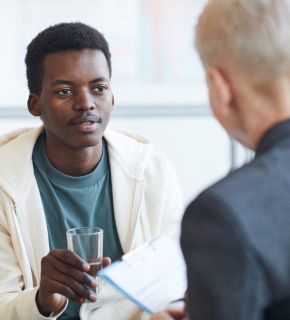 A young man wearing a hoodie is seen speaking to his counselor