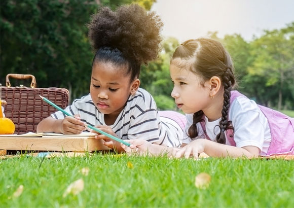 Two elementary school girls work on a project in the grass during summer session