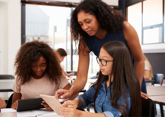 A teacher leans over two students as they do their work in their elementary special education classroom