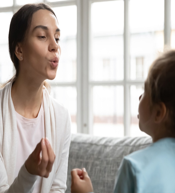A speech therapist models forming words for a young child