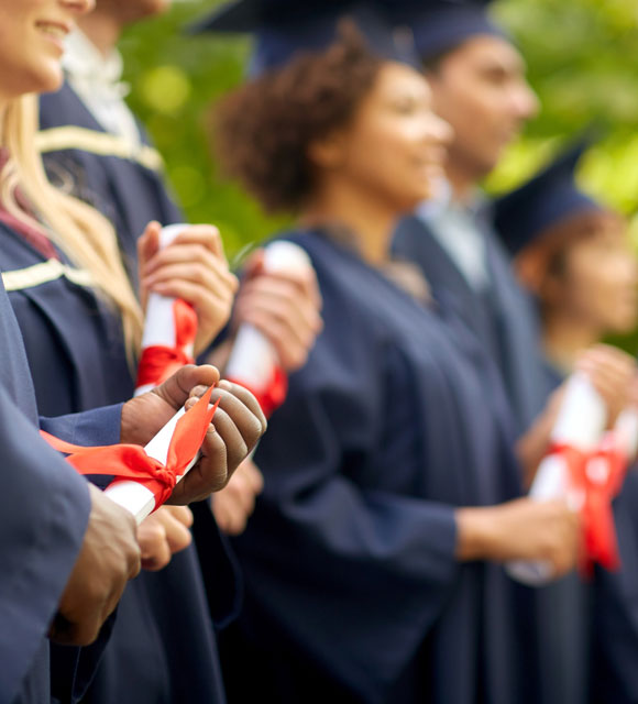 A group of high school graduates hold diplomas at an outside ceremony