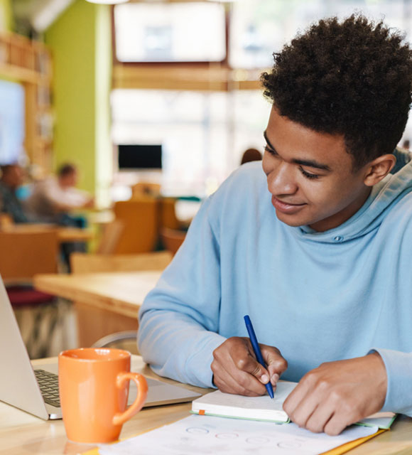 A high school student works on his computer with a cup of coffee