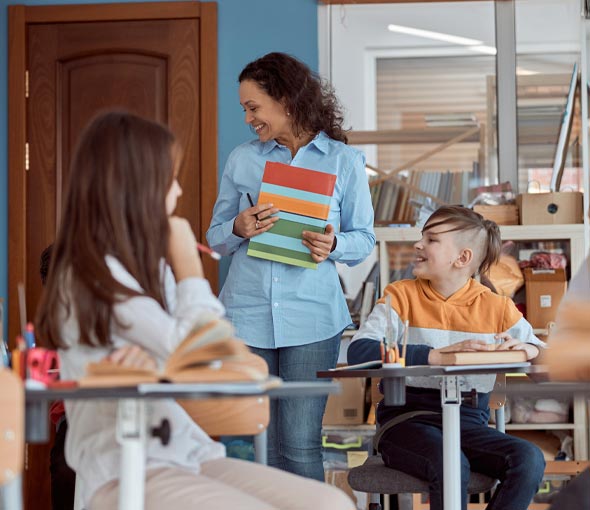 A special education teacher works with her students while holding a brightly colored folder